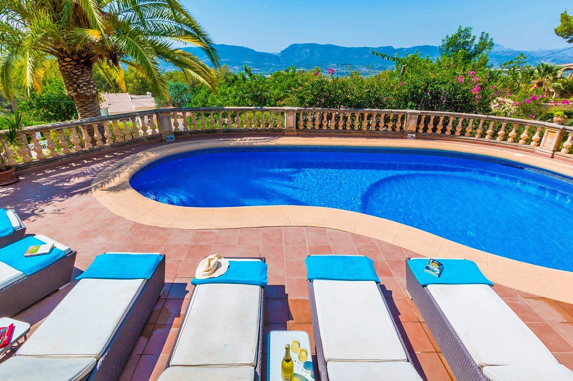 A curved swimming pool with lounge chairs and a view of mountains.
