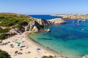 Una playa con aguas turquesas cristalinas, afloramientos rocosos y varios barcos.