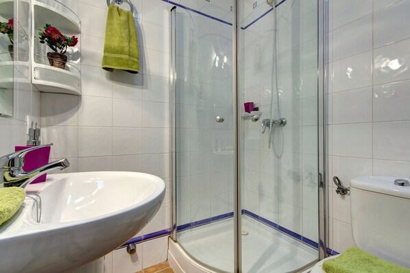 Un baño con ducha de vidrio, lavamanos blanco y un inodoro.