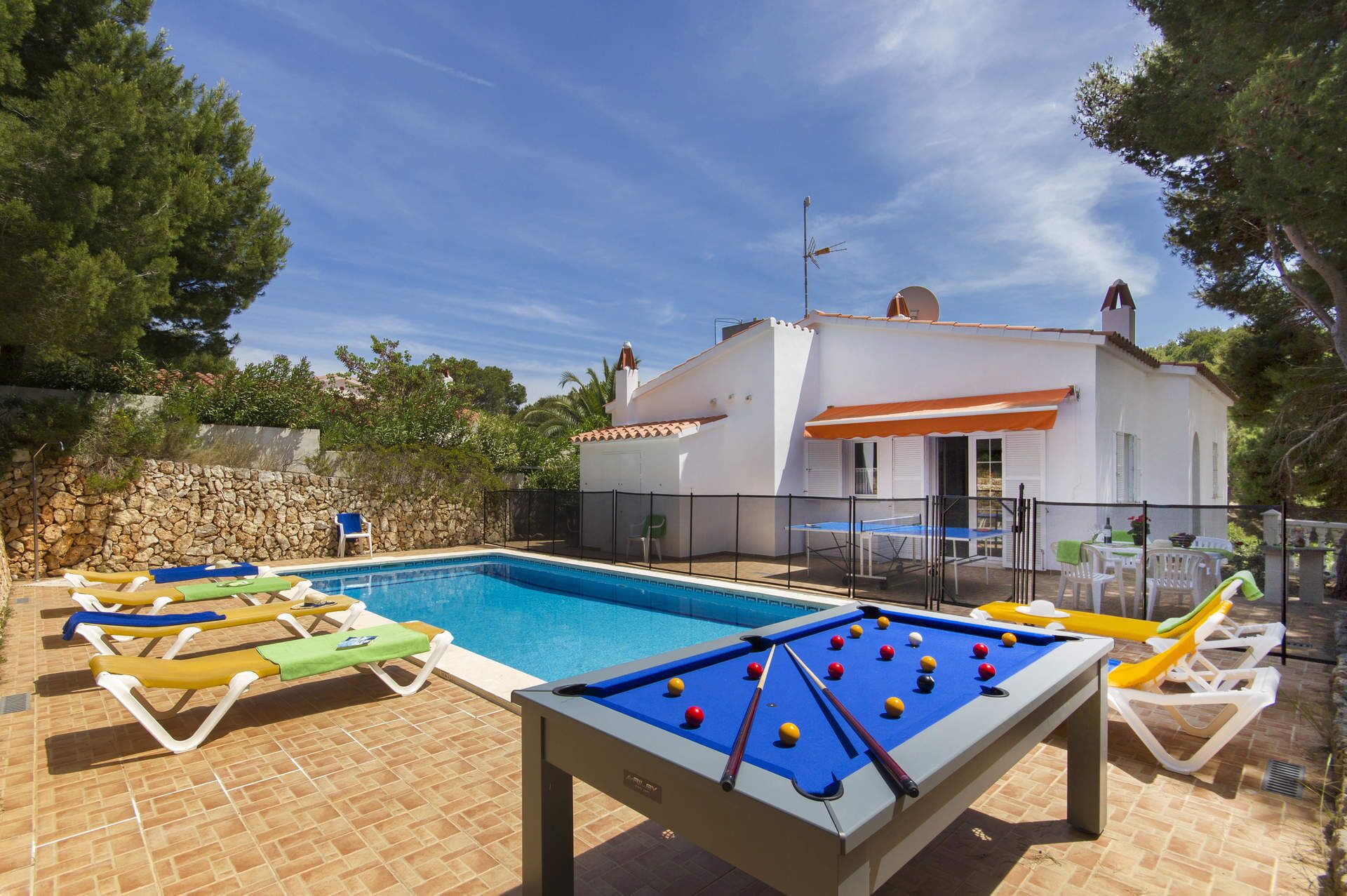A pool area with lounge chairs, a foosball table, and a building with a tiled roof.