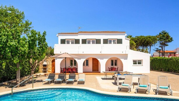 Una casa moderna de dos pisos con piscina, mobiliario exterior y chimenea de piedra.
