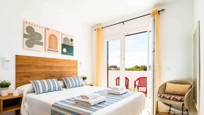 Un dormitorio moderno con cabecera de madera, una cama grande con ropa de cama a rayas, una mesita de noche pequeña con una planta y vistas al exterior a través de una puerta corrediza de vidrio.
