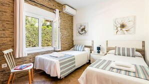 Un dormitorio con dos camas, una ventana con cortinas, una silla y una mesita de noche con lámpara.