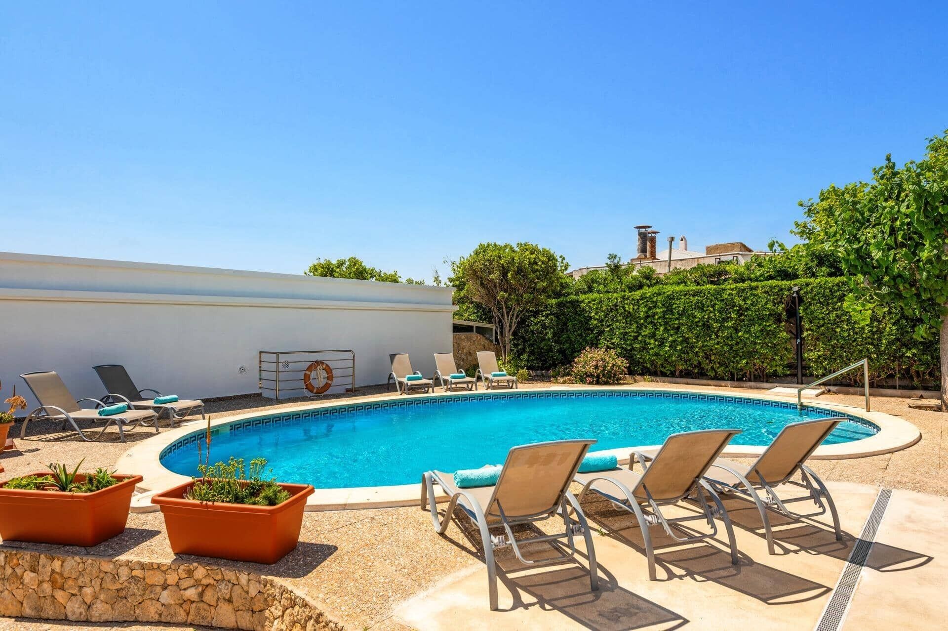 A swimming pool with lounge chairs and potted plants, surrounded by a stone wall and greenery.