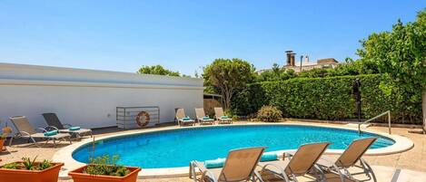 A swimming pool with lounge chairs and potted plants, surrounded by a stone wall and greenery.