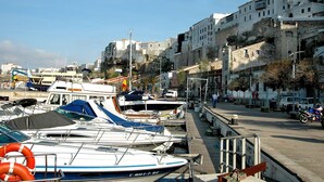 Una marina con barcos amarrados, una calle con edificios y un cielo despejado.