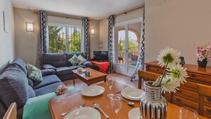 Ein Wohnzimmer mit einer Couch, einem Couchtisch und einem Esstisch für zwei Personen, gedeckt mit Tellern, Gläsern und Besteck.