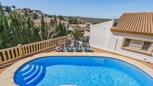Ein Swimmingpool mit Sonnenterrasse, Liegestühlen und Blick auf die umliegende Gegend.