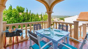 Ein Balkon mit Tisch für zwei Personen, einem Grill und Blick auf Grünflächen und Gebäude.