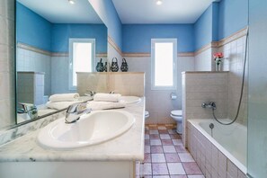 A bathroom with a marble sink, two toilets, a bathtub, and blue walls.