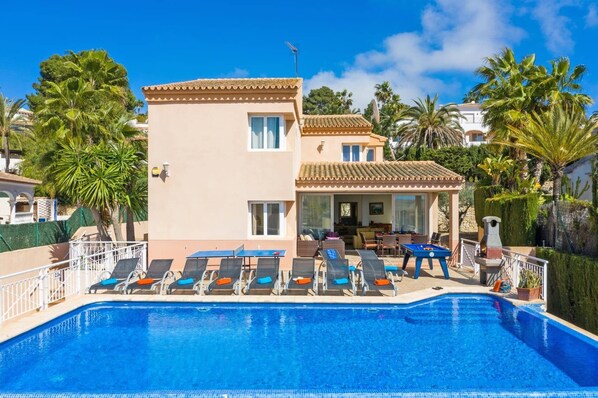 A poolside area with lounge chairs, a pool, and a building with a tiled roof and windows.