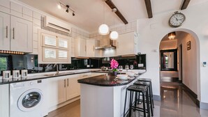 Una cocina moderna con armarios blancos, una isla central con taburetes y lavadora integrada, además de iluminación colgante.