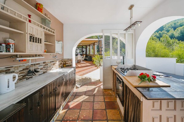 A modern kitchen with a stone backsplash, wooden cabinets, and a view of a lush garden through an archway.