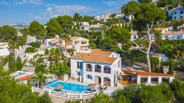 Una villa costera con piscina, rodeada de exuberante vegetación y otras edificaciones residenciales.