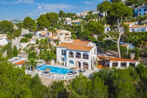 A coastal villa with a swimming pool, surrounded by lush greenery and other residential buildings.