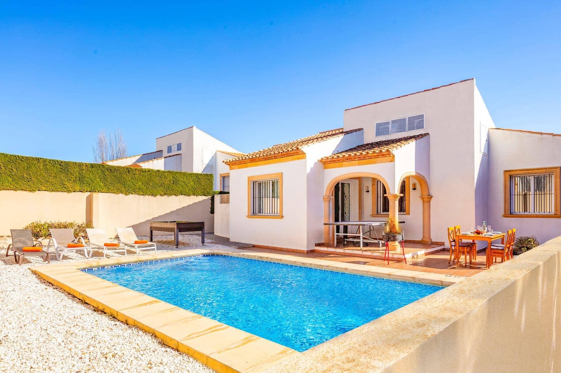 A poolside area with a swimming pool, lounge chairs, and a dining table.