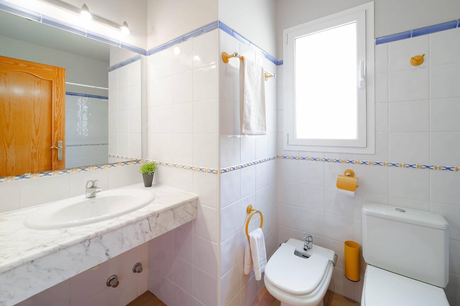 Een badkamer met een marmeren wastafel, toilet en raam.