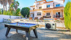 A pool area with a table tennis table, outdoor seating, and a large house with a tiled roof. - Villa Belinda by Villa Plus (Calp)