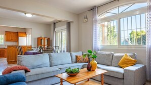 A spacious living room with a grey sofa set, a wooden coffee table, and a view of the kitchen in the background. - Villa Belinda by Villa Plus (Calp)
