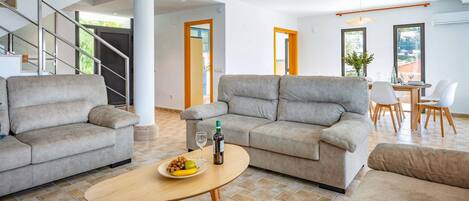 A spacious living area with a sofa set, a dining table, and a staircase.