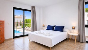 A hotel room with a bed, two bedside tables, a view of a pool and greenery, and a sliding glass door. - Villa Catorce Flores by Villa Plus (Teulada)