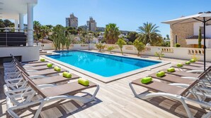 A swimming pool with lounge chairs and towels, surrounded by greenery and buildings in the background. - Villa Catorce Flores by Villa Plus (Teulada)