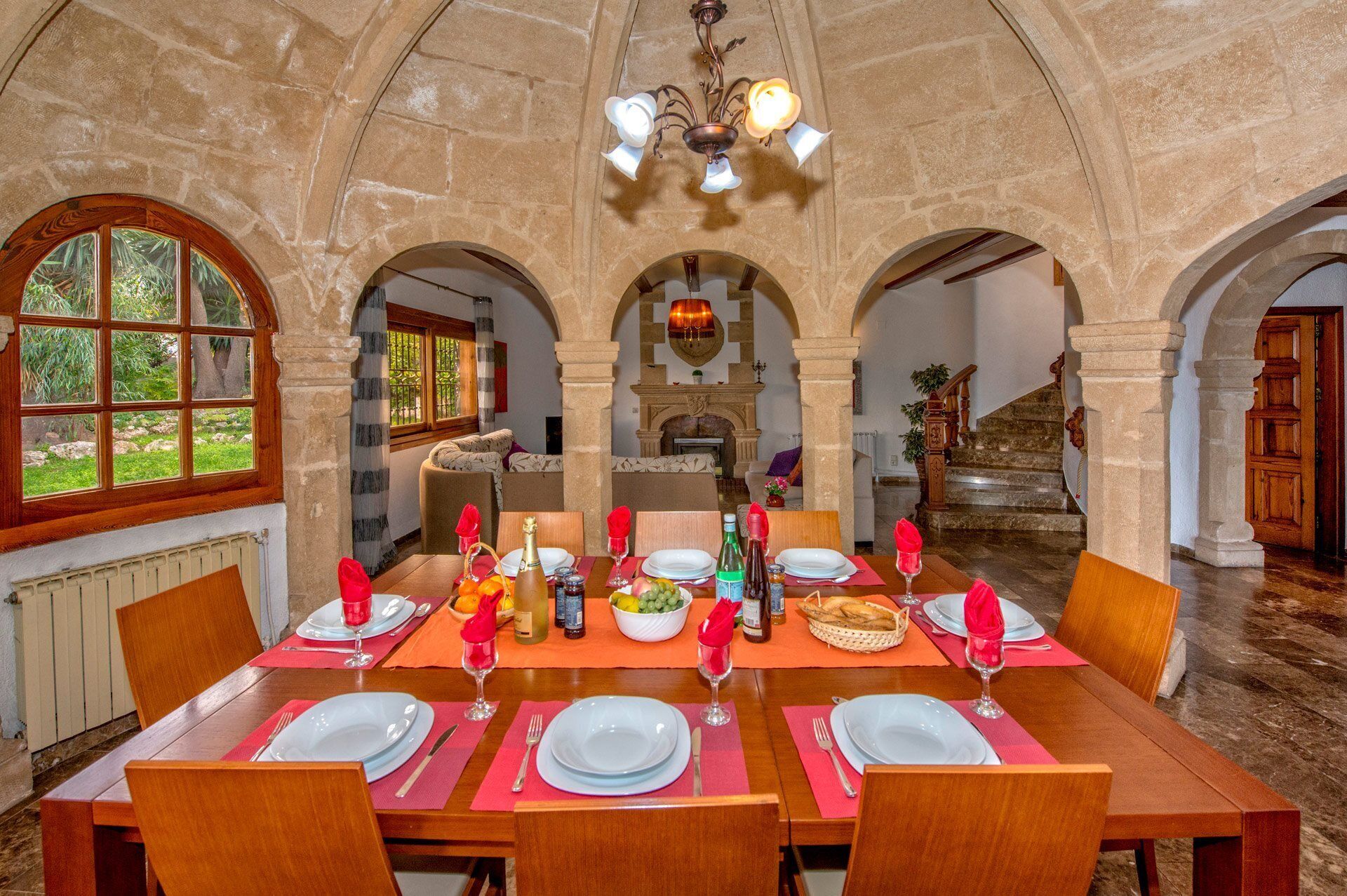 Un espace repas doté d’un plafond en forme d’arc en pierre, d’une cheminée et d’une vue sur un jardin, visible à travers une fenêtre.