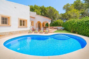 A swimming pool with lounge chairs, a covered patio, and a white building with arches.