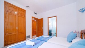 A bedroom with a large wooden wardrobe, a bed with blue and white bedding, and a bathroom visible through an open door. - Villa Ciruela by Villa Plus (El Tosalet)