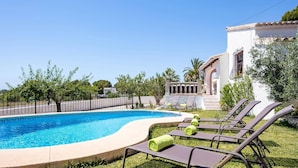 Uma piscina com espreguiçadeiras e um edifício branco com telhado em azulejos.