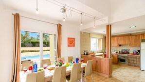 A modern kitchen with wooden cabinets, a central island, and a dining area with a table set for six. - Villa Elefante by Villa Plus (Jávea)