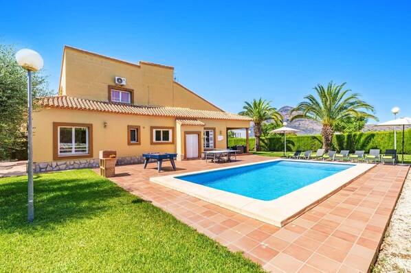 Ein zweigeschossiges Haus mit Swimmingpool, Außenbereich zum Sitzen und einem gepflegten Garten.