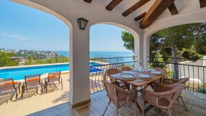 Eine Terrasse mit Pool, Esstisch und Stühlen mit Blick auf die Küste.