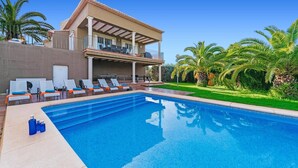 Une maison moderne avec une piscine, des chaises longues et des palmiers.