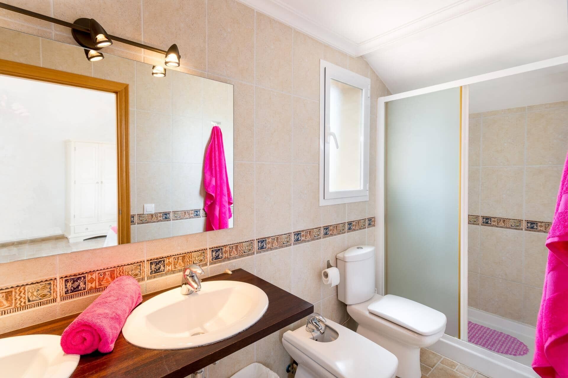 A bathroom with a sink, mirror, toilet, and shower.