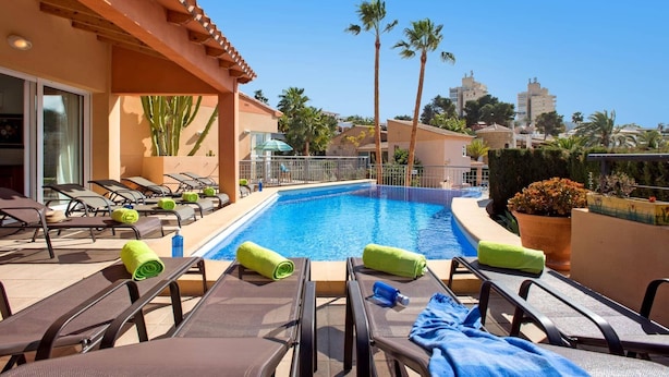 A poolside area with lounge chairs, a swimming pool, and palm trees. - Villa Mar Flores by Villa Plus (Teulada)