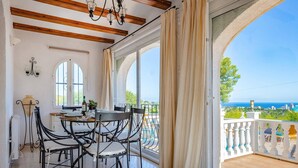A dining area with a table and chairs, large windows, and a view of the sea. - Villa Moggalatto by Villa Plus (Calp)