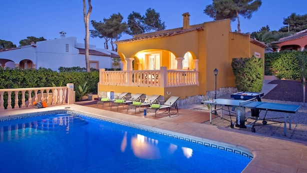 Un área de piscina con sillones reclinables, una mesa y un edificio con balcón.