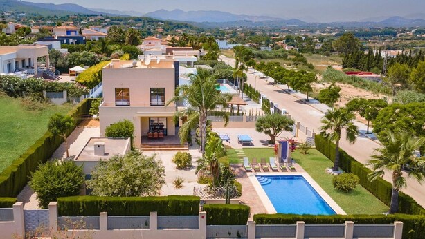 Una villa moderna con piscina, varios balcones y un jardín bien cuidado.