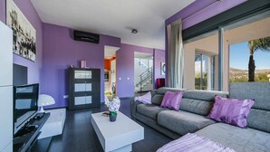 Una sala de estar moderna con un sofá gris, una mesa de centro blanca y detalles morados.