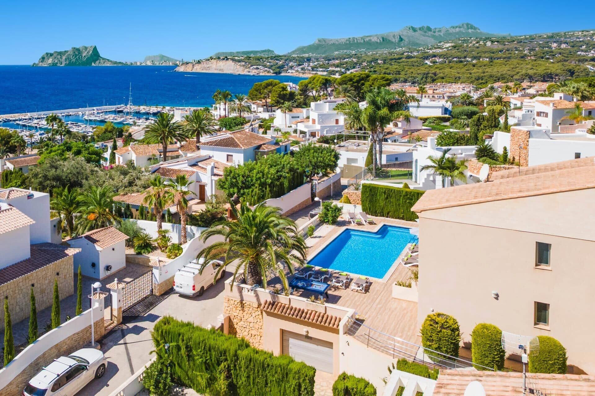 A coastal residential area with a swimming pool, white buildings, and a view of the sea.