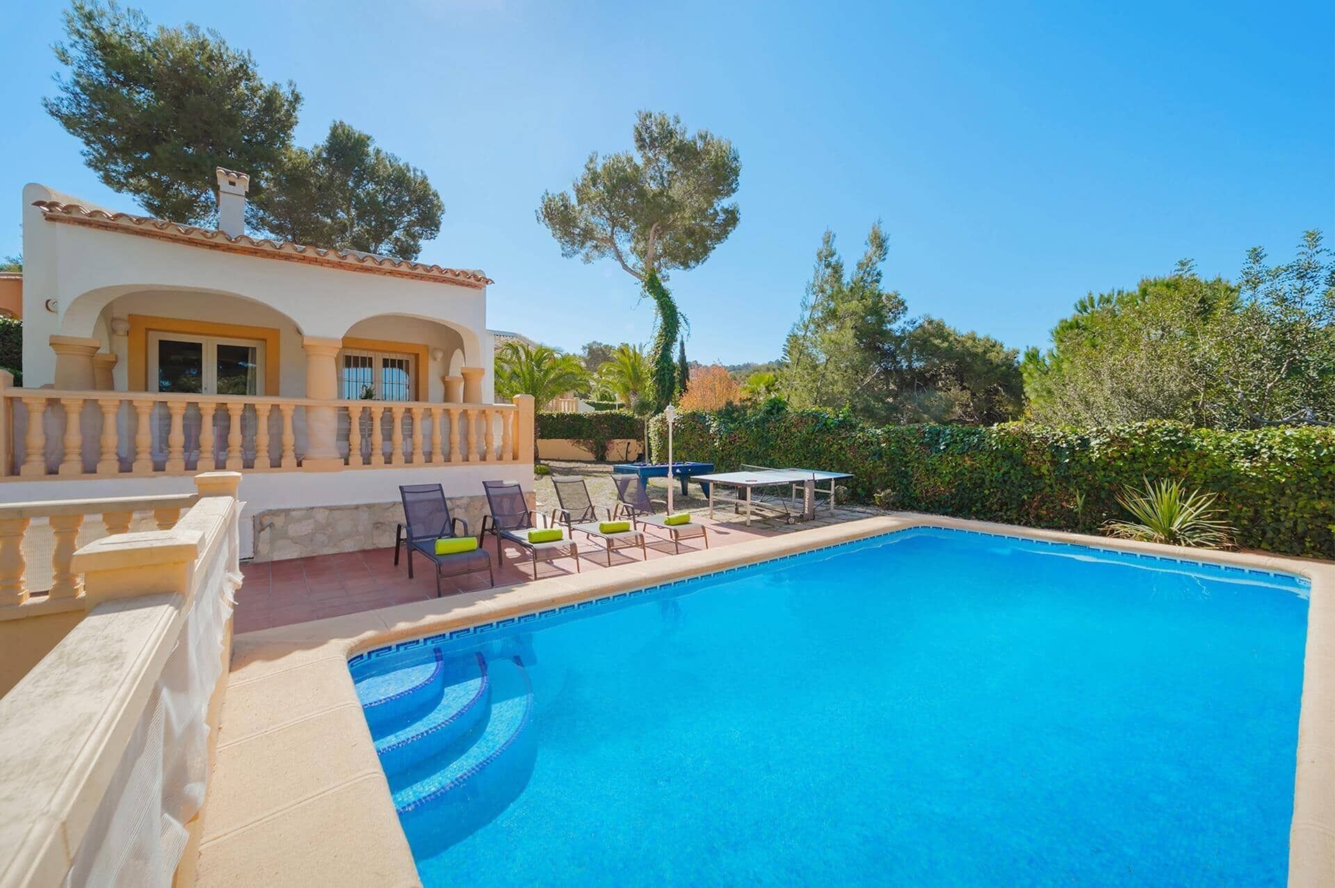 Une piscine avec une terrasse carrelée, des espaces de détente en plein air et un bâtiment doté d’un balcon.