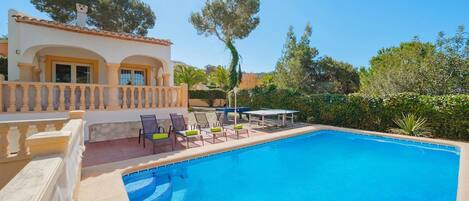 Une piscine avec une terrasse carrelée, des espaces de détente en plein air et un bâtiment doté d’un balcon.