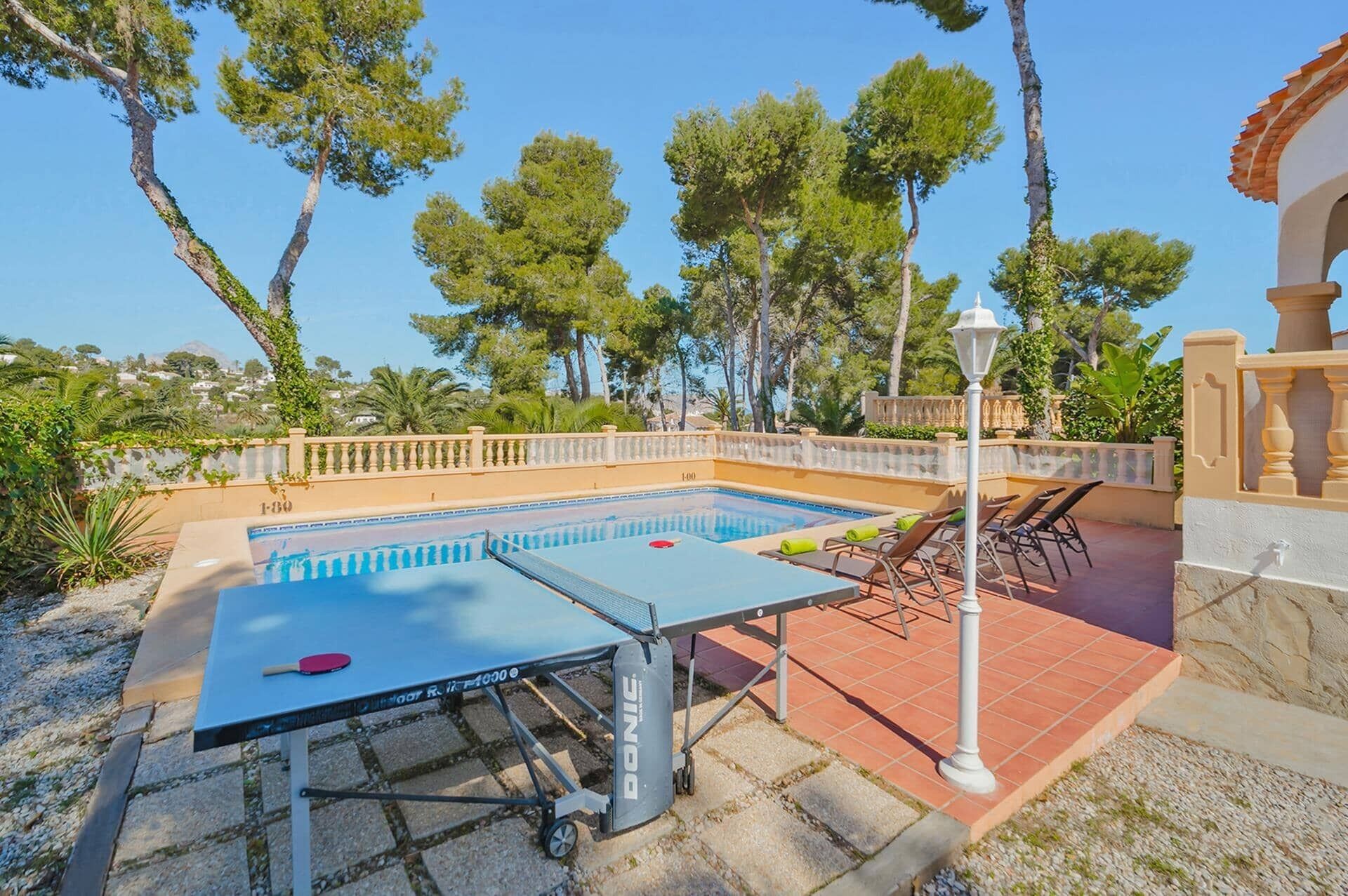 An outdoor pool area with a table tennis table, lounge chairs, and a lamp post.
