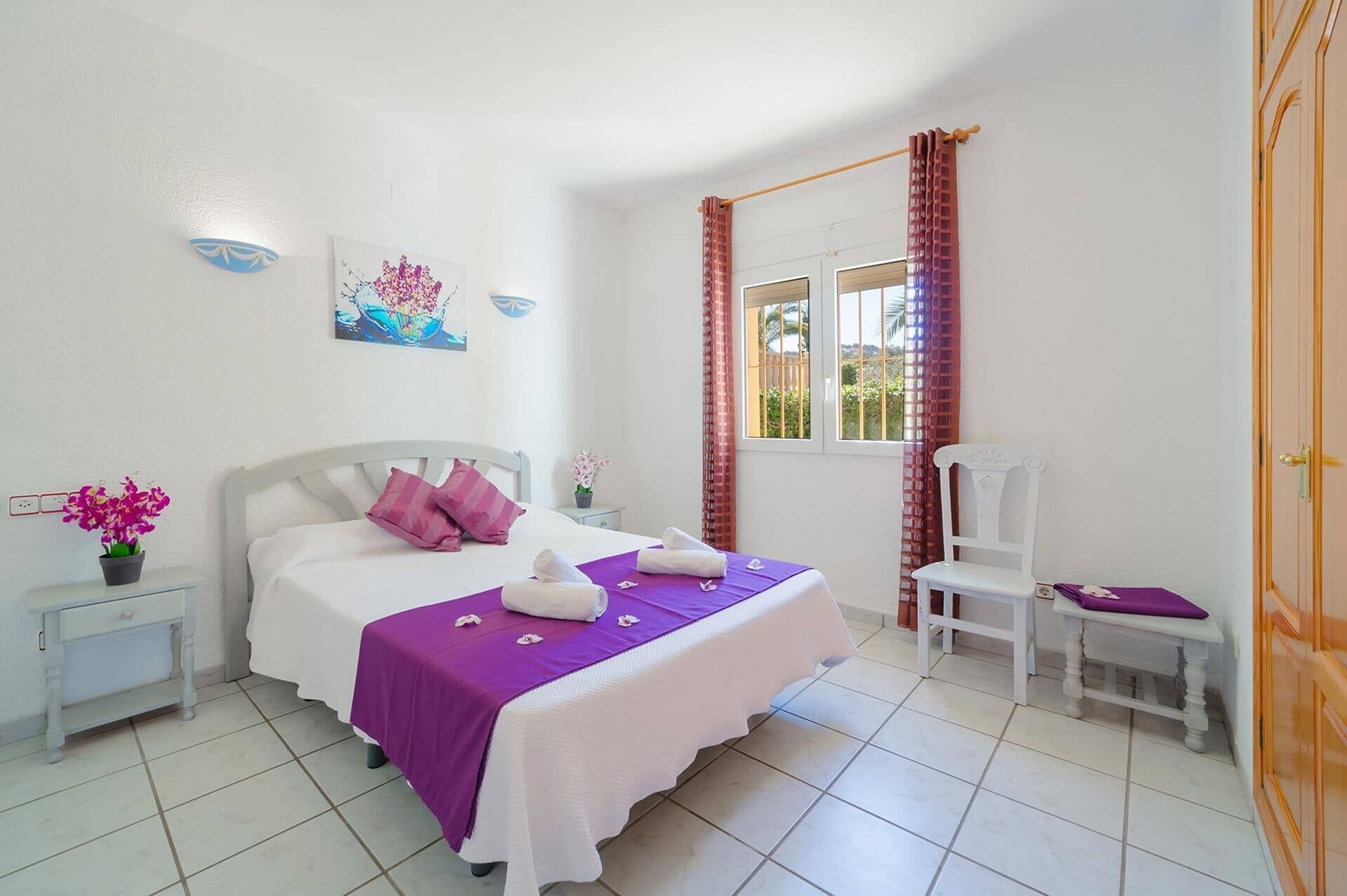 A bedroom with a bed, a chair, a nightstand, a window with curtains, and a door.