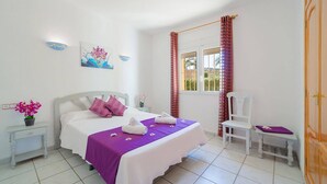 A bedroom with a bed, a chair, a nightstand, a window with curtains, and a door. - Villa Rosa Blanca by Villa Plus (El Tosalet)