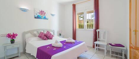 A bedroom with a bed, a chair, a nightstand, a window with curtains, and a door.