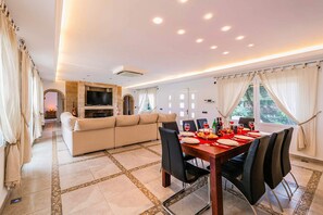 A modern living room with a dining area, a sofa, and a TV mounted on the wall. - Villa Silvasol by Villa Plus (Javea)