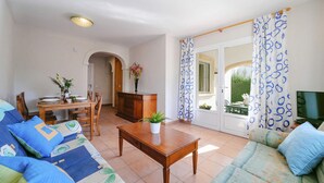 Una sala de estar con un sofá, una mesa de comedor para dos personas, un aparador de madera y un televisor sobre un mueble.