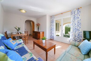 Un salon comprenant un canapé, une table à manger dressée pour deux personnes, un meuble en bois et un téléviseur posé sur un meuble.
